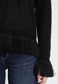 Černý pletený svetr s texturovaným třásněním na spodním okraji a manžetách. Má pohodlný střih a měkkou tkaninu. Vhodný pro běžné nošení.