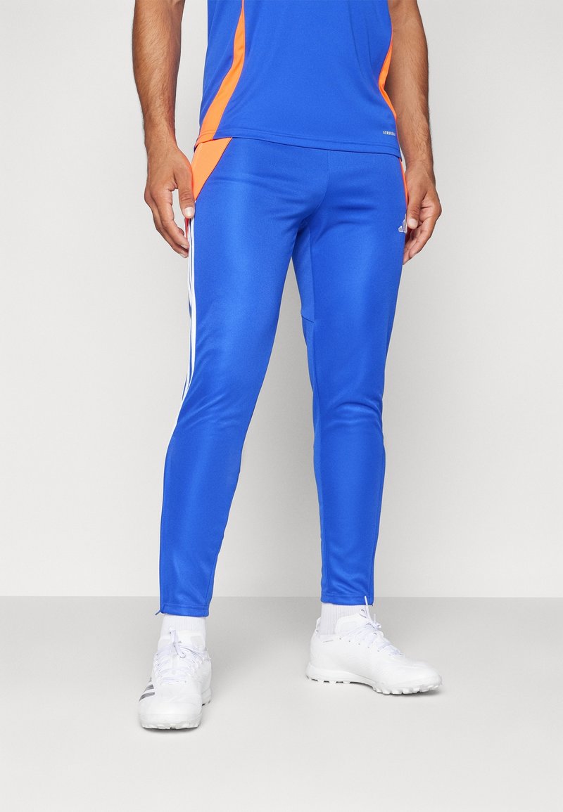 Pantalon de sport bleu avec une coupe ajustée, présentant des accents latéraux orange et des rayures blanches sur les côtés. Fabriqué dans un matériau lisse et extensible.