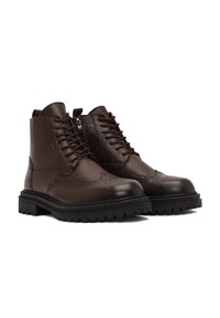 Bottes de cheville en cuir marron avec un design à lacets, des détails brogue et une finition texturée. Elles comportent une épaisse semelle en caoutchouc noir et une fermeture éclair.