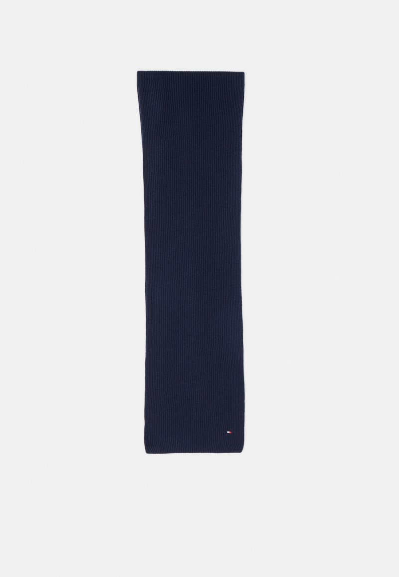 Écharpe en tricot bleu marine, de forme rectangulaire, en tissu texturé à côtes, avec un petit logo rouge, blanc et bleu près de l'extrémité.