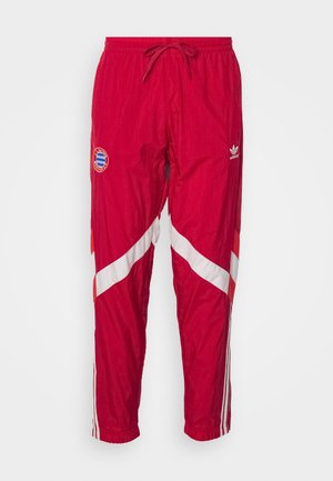 Pantalones deportivos rojos con rayas diagonales blancas y rojas, puños elásticos y cintura con cordón ajustable. Presenta un logo circular y un pequeño emblema de la marca.