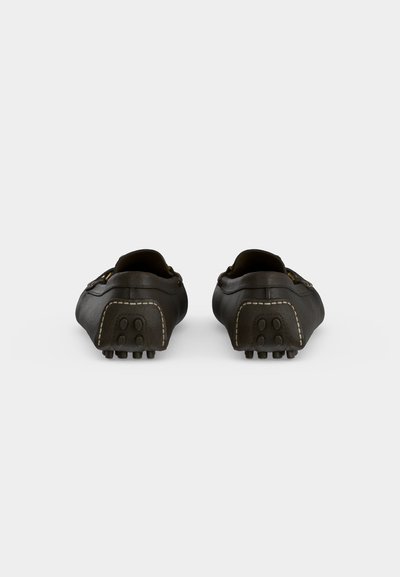 Paire de chaussures de conduite en cuir noir vues de dos avec des grips en caoutchouc visibles sur les talons et des coutures contrastées.