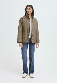 Quiltad brun jacka med tryckknappar, hög krage och sidofickor. Tillsammans med blå jeans och vita sneakers. Enfärgad, minimal design.