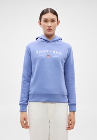 Sudadera con capucha azul de algodón con un logo gráfico frontal "GANT1949" y un emblema de escudo. Los puños y el dobladillo son acanalados.