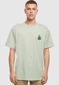 Hellgrünes Baumwoll-T-Shirt mit einem kleinen grünen Weihnachtsbaum-Graphic auf der linken Brust. Lässiger Schnitt mit kurzen Ärmeln.