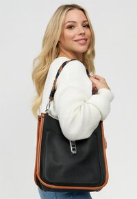 Zwarte leren handtas met oranje accenten en een gestructureerde afwerking, voorzien van een zilveren sluiting en een patronen schouderriem.