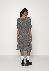 Vestido preto com estampado floral, mangas bufantes, cintura ajustada e saia em camadas. Detalhe nas costas em forma de fenda. Combinado com botas pretas e meias brancas.