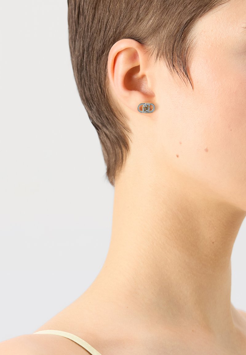 Orecchino a spillo in argento con un design geometrico che presenta forme interconnesse, superficie liscia e finitura lucida, indossato da un modello con capelli corti.
