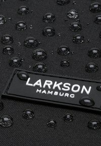 Fekete textúrájú szövet vízcseppekkel; egy téglalap alakú fekete címke látható rajta, amelyen fehér betűkkel az olvasható: "LARKSON HAMBURG".