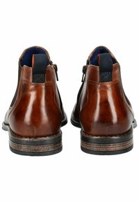 Bottines en cuir marron avec une finition lisse, dotées d'une fermeture éclair sur le côté, d'accents en tissu et d'une semelle noire légèrement texturée.