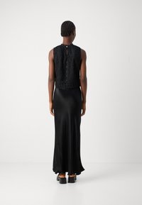 Czarna koronkowa bluzka z wysokim kołnierzem, nałożona na gładką, lejącą czarną satynową spódnicę. Charakteryzuje się delikatnym rozcięciem z tyłu i luźnym krojem.