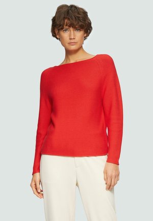 Pull en tricot rouge avec un décolleté bateau, des manches longues et un motif texturé. Assorti à un pantalon crème.