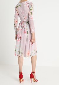 Kukallinen midi-mekko vaaleanlilassa värissä, jossa on pitkät hihat, pleiattu hame ja takana vetoketju. Mekossa on vaaleanpunaisia ja vihreitä kukkakuoseja.