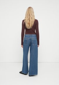 Jeans de mezclilla de pierna ancha en azul, con un diseño clásico de cinco bolsillos y una cinturilla alta, combinados con una blusa ajustada de manga larga marrón.
