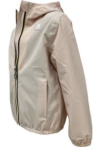 Giacca impermeabile beige chiaro con cappuccio, polsini elastici, chiusura frontale con zip e dettagli gialli, e un piccolo logo sul petto.