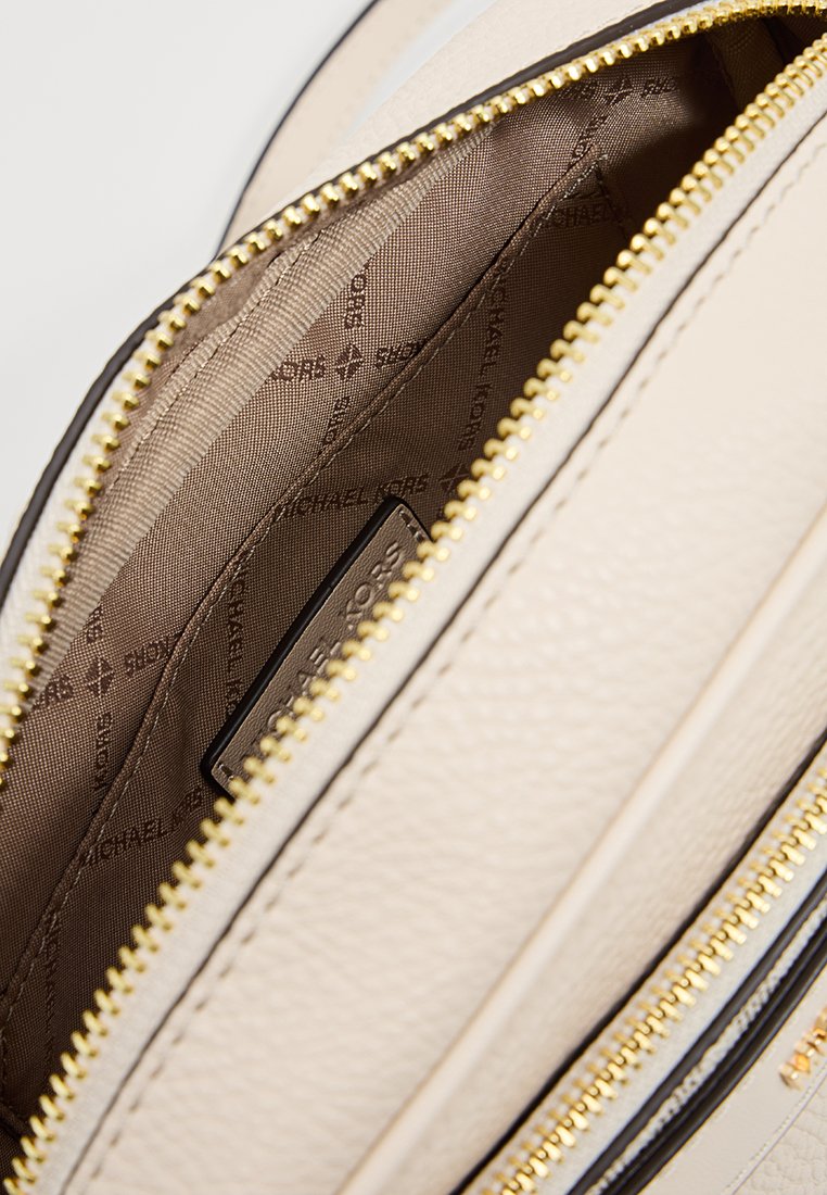 Beiger Lederhandtascheninnenraum mit glatter Textur, ausgestattet mit goldfarbenem Reißverschluss und einem monogrammierten Innenfutter in warmer Braunnuance.