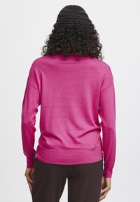 Rosa stickad tröja med avslappnad passform, långa ärmar och ribbade muddar. Slät textur och subtil lyster; bakvy visar en enkel design.