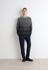 Maglione grigio ombré lavorato a maglia con una texture a coste, abbinato a pantaloni navy scuri e scarpe di cuoio nere per un look elegante e moderno.