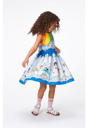 Robe colorée avec un corsage arc-en-ciel, une taille bleue et un imprimé de manège ludique. Elle présente une jupe évasée et des sandales blanches assorties.