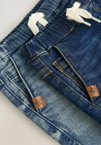 Shorts en denim de deux teintes : bleu clair et bleu foncé. Les caractéristiques incluent une taille à cordon, des détails de couture et des accents en cuir avec des étoiles.