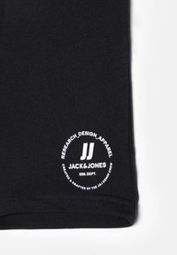 Svart bomull t-shirt med en cirkulär vit logotyp som har texten "JACK & JONES" och "RESEARCH_DESIGN_APPAREL". Slät textur och korta ärmar.