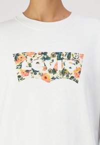 Biela mikina s kvetinovým logom Levi's v odtieňoch ružovej, modrej a zelenej, umiestneným na prednej strane. Mäkká textúra, okrúhly výstrih.