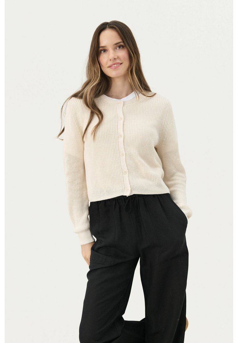 Licht beige geribde cardigan met ronde hals en knoopsluiting, gecombineerd met losse zwarte broek. Getextureerde stof, aansluitende mouwen, cropped ontwerp.