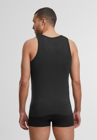 Černý tílko, přiléhavý design, vyrobené z hladkého materiálu. Má široké ramínka a kulatý výstřih, spárované s černými šortkami.