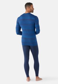 Blauwe langarmshirt met een gestructureerd gestreept patroon, gecombineerd met marineblauwe leggings. Het shirt heeft een ronde halslijn en een getailleerde pasvorm.