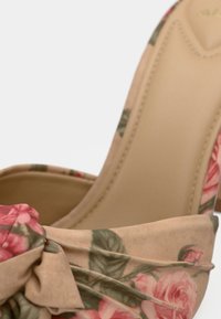 Zapato cerrado tipo tacón hecho de tela con estampado floral en tonos rosas y verdes, con un lazo de tela y una plantilla lisa de color claro.