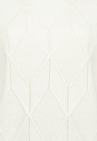 Bílá pletená tkanina se zvýšenými vzory ve tvaru diamantů v texturovaném, opakujícím se geometrickém designu.