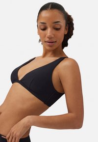 Bralette negra con un diseño de escote en V profundo, tirantes anchos y textura suave. Silueta simple y elegante con un detalle mínimo.