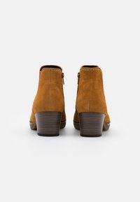 Botas de tobillo de gamuza color beige con un acabado texturizado, un tacón de madera y un cierre lateral. Un doble cosido destaca el diseño.