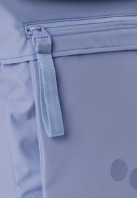 Hellblauer Rucksack mit einem oberen Reißverschluss, strukturierter Stoff, einem flachen Tragegurt und zwei runden Akzenten an der Seite.