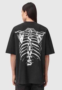 Zwart katoenen T-shirt met een grote witte ribbenkastafbeelding op de achterkant, met de tekst "ALL SAINTS" geïntegreerd in het ontwerp.