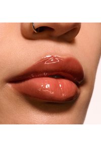 Labbra lucide e piene in una delicata tonalità pesca, con una texture liscia e una leggera brillantezza. I piercing al naso accentuano i tratti del viso.