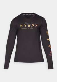 Maglietta sportiva nera a maniche lunghe con logo "HYROX" in gradiente arancione e giallo, con ulteriore branding sulle maniche e nel colletto.