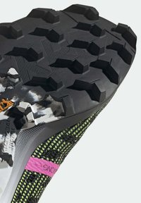 Czarne i zielone buty sportowe z textured cholewką, różowymi detalami i wytrzymałą czarną gumową podeszwą z heksagonalnymi wypustkami dla lepszej przyczepności.