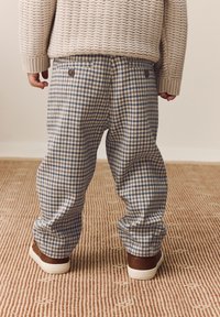 Kollade blå och beige byxor med avslappnad passform, utrustade med två bruna knappar på bakfickorna, tillsammans med bruna sneakers.
