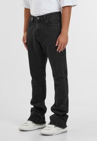 Zwarte denim jeans met een rechte pasvorm, vijf zakken en een klassieke knoopsluiting. G gedragen met witte sneakers.