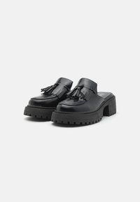 Zwarte leren platform mules met franjes, vierkante neus en dikke, gestructureerde zolen. Voorzien van een lage blokhak en gedetailleerde stiksels.