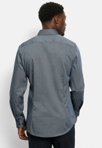 Langärmliges Hemd in Marineblau mit geometrischem Muster, Button-Down-Kragen und kontrastierenden Knopfdetails an den Manschetten. Weiches, strukturiertes Material.