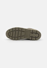 Suela de goma verde oliva con surcos profundos para tracción. Superficie texturizada con un detalle del logo rectangular. Diseño duradero y resistente.