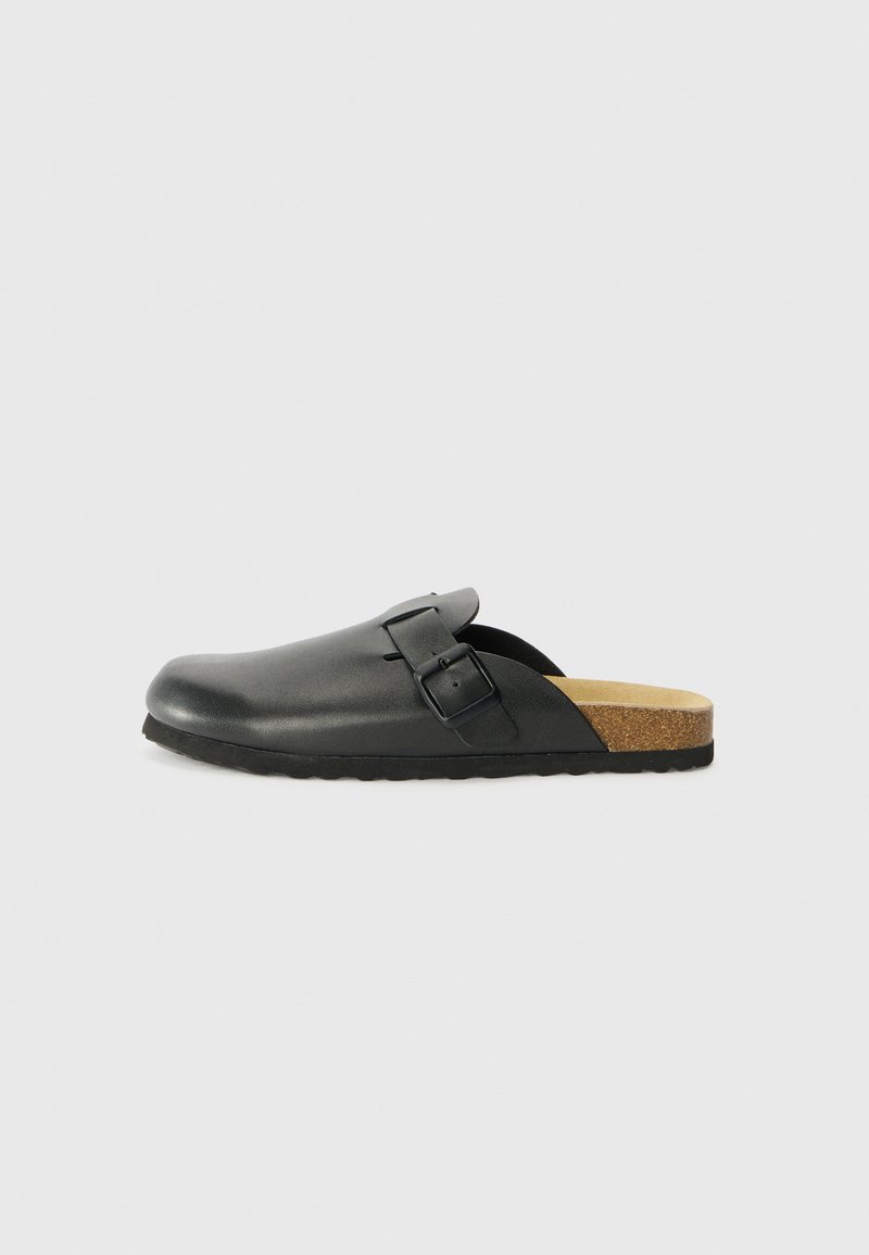 Black leather clogs with a rounded toe, a strap and buckle detail, and a cork footbed, featuring a textured rubber sole.