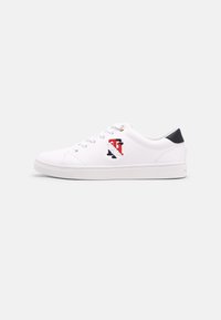 White sneaker with a smooth leather texture, featuring a blue and red embroidered logo on the side and a black accent at the heel.