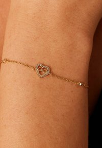 Gouden armband met een hartvormige bedel met een oneindigheidssymbool, versierd met heldere kristallen, weergegeven op een pols.