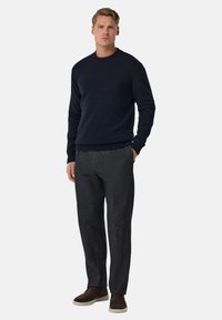 Námořnicky modrý pletený svetr s žebrovaným kulatým výstřihem, doplněný tmavými vzorovanými kalhotami a hnědými semišovými botami. Jednoduchý, moderní design.