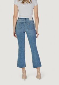 Vaqueros de mezclilla azul acampanados con cintura alta, bolsillos traseros y un dobladillo sin terminar. Combinados con una blusa blanca ajustada y zapatos de tacón nude.