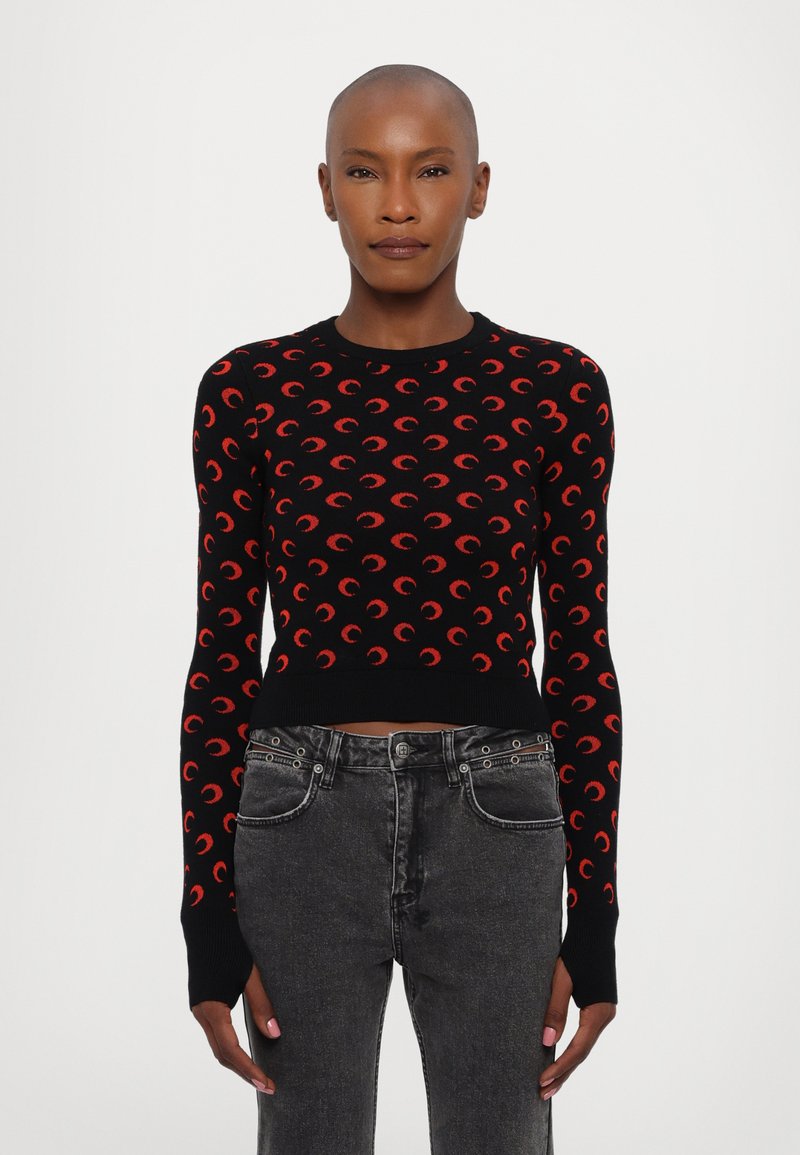 Černý svetr s červenými vzory srpku, přiléhavý střih, žebrované manžety a lem. Kombinováno s černými džíny s vysokým pasem.