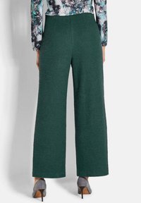 Grüne strukturierte weite Hosen mit hoher Taille, von hinten gezeigt. Das Model trägt graue Absätze, die die Hosenlänge betonen.